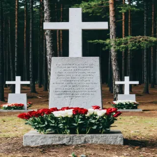 "A memorial in modern Poland: stone monuments and crosses in the Katyn forest, surrounded by grieving families laying flowers."